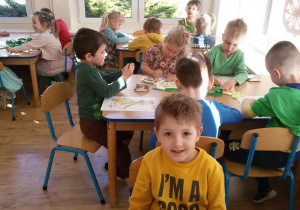 Widok na siedzące przy stolikach dzieci, które kolorują żonkile.